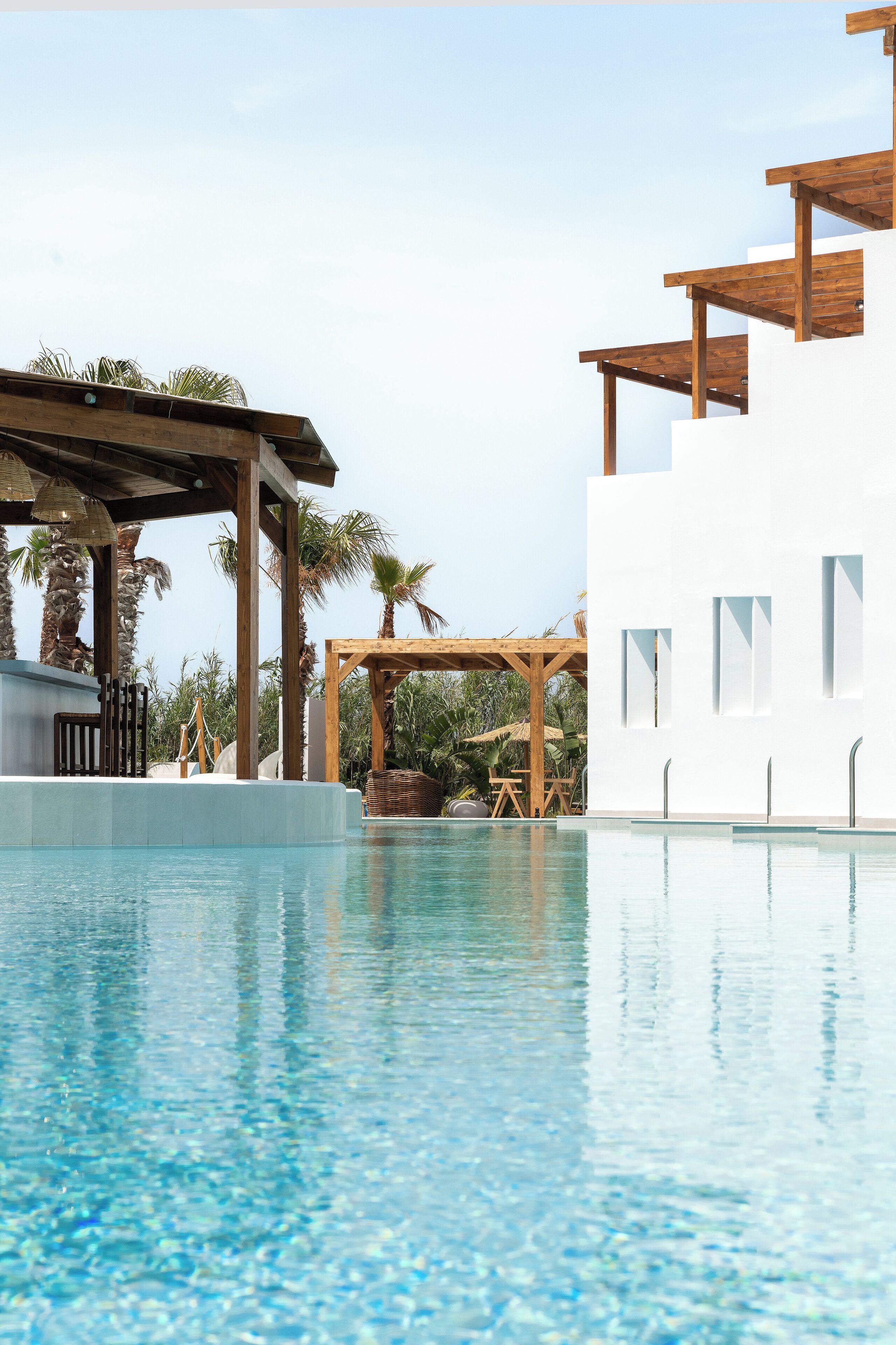 A modern pool area with clear water, wooden pergolas, and white buildings.