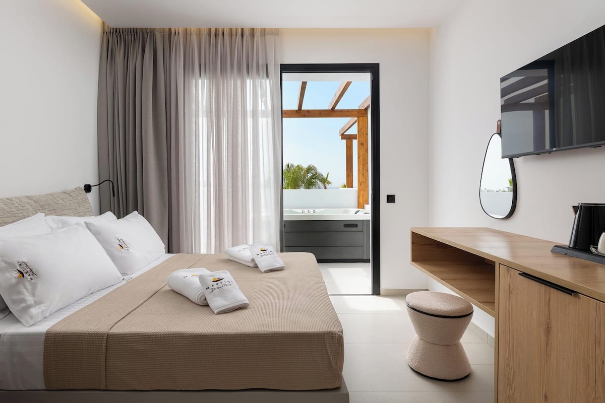 A modern hotel room with a bed, a wooden desk, a flat-screen TV, and a view of the outside balcony.
