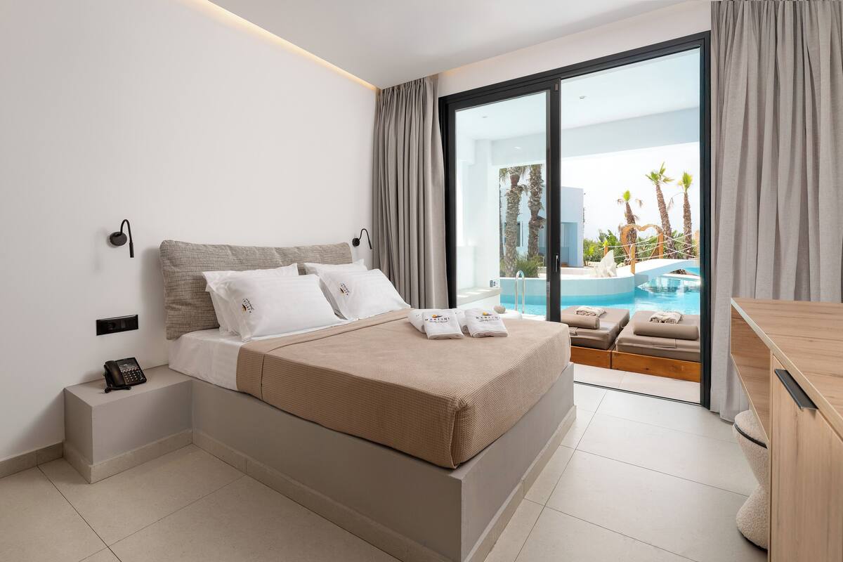 A modern hotel room with a large bed, a bedside phone, and a view of a swimming pool and palm trees.
