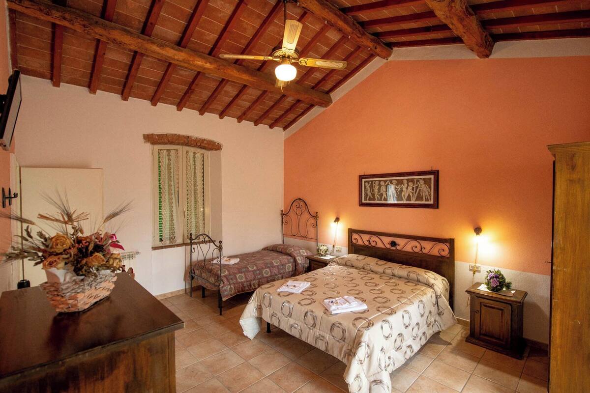 A bedroom with two beds, a wooden ceiling, a window with curtains, a painting on the wall, and a bedside table with a lamp.