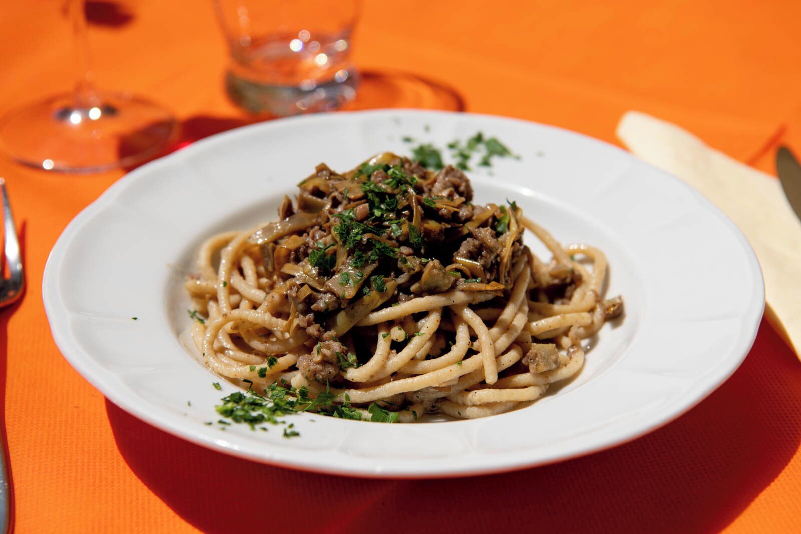 Een bord spaghetti met vlees en champignons, versierd met kruiden, op een wit bord.