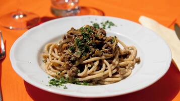 Een bord spaghetti met vlees en champignons, versierd met kruiden, op een wit bord.