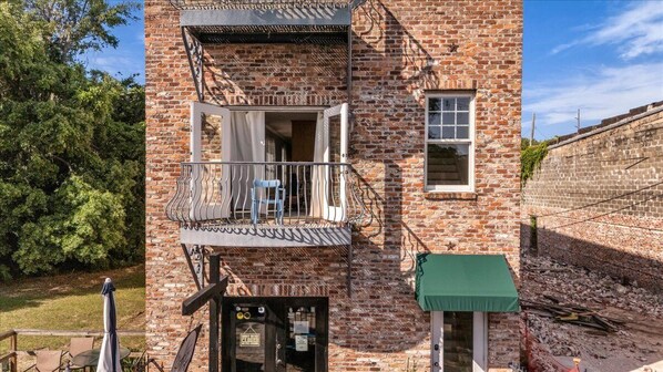 A brick building with a balcony, a window, and a green awning. - Cozy 2bed, 2bath loft in downtown Darien, GA! Enjoy a master room with a balcony view of the river. (Darien)
