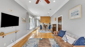 A spacious living room with a large flat-screen TV, a ceiling fan, and a wooden floor. - Cozy 2bed, 2bath loft in downtown Darien, GA! Enjoy a master room with a balcony view of the river. (Darien)
