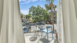 A balcony with a table and chairs, overlooking a street with parked cars and trees. - Cozy 2bed, 2bath loft in downtown Darien, GA! Enjoy a master room with a balcony view of the river. (Darien)