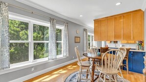A dining area with a wooden table and chairs, a blue and white patterned rug, and large windows with curtains. - Cozy 2bed, 2bath loft in downtown Darien, GA! Enjoy a master room with a balcony view of the river. (Darien)