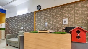 A reception desk with a clock above it, a red birdhouse, and a patterned wall.