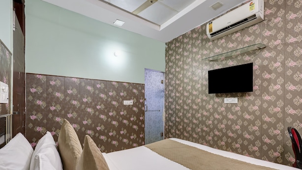 A hotel room with a bed, pillows, a TV mounted on the wall, and an air conditioning unit.
