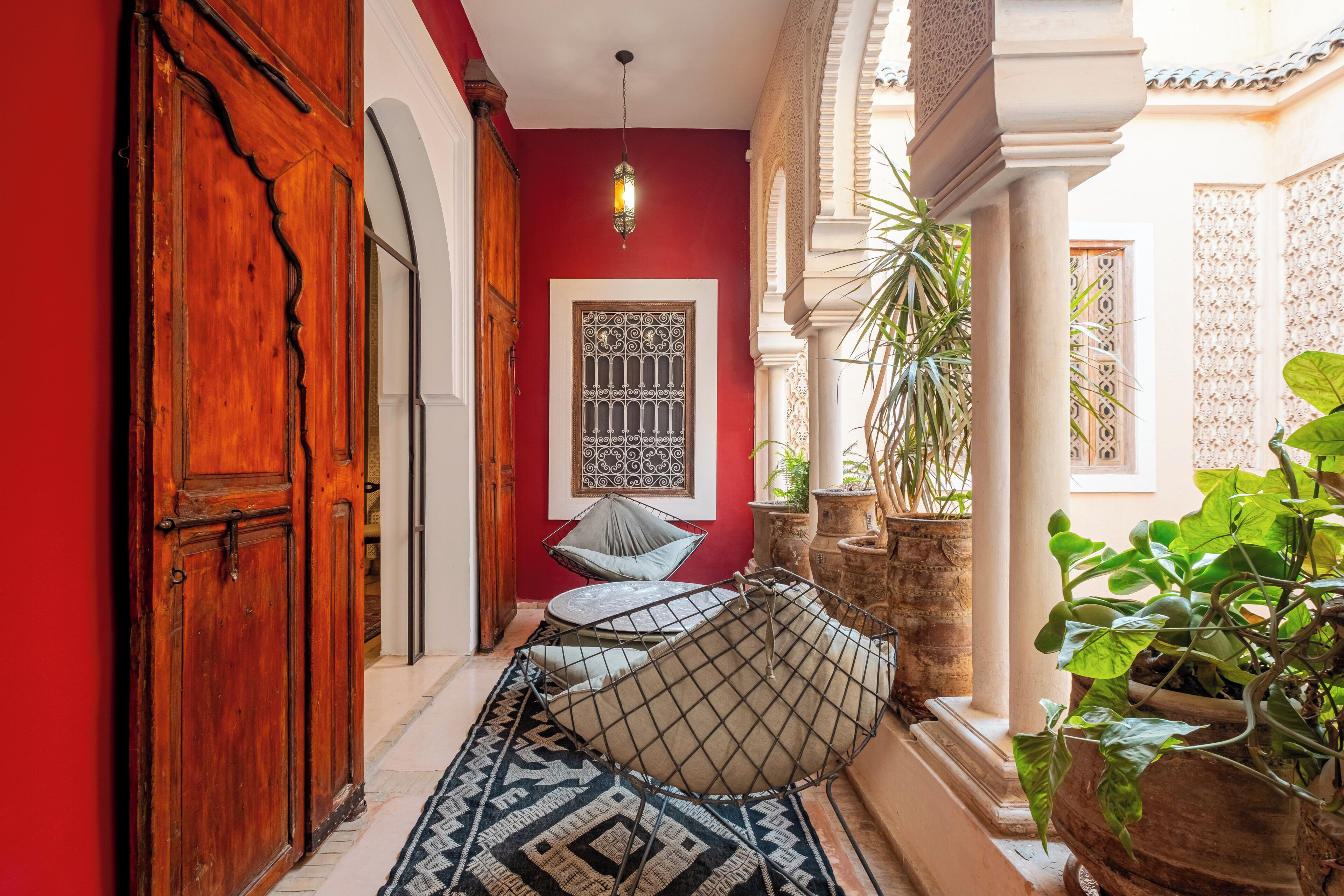 A corridor with a red wall, a patterned door, a hanging light fixture, and a patterned rug.