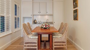 Ein Essbereich mit Holztisch, Korbstühlen, weißen Schränken und einer Blumenarrangements.