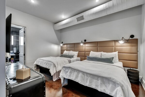 Una habitación de hotel moderna con dos camas, un tocador con espejo y una maleta en el suelo.