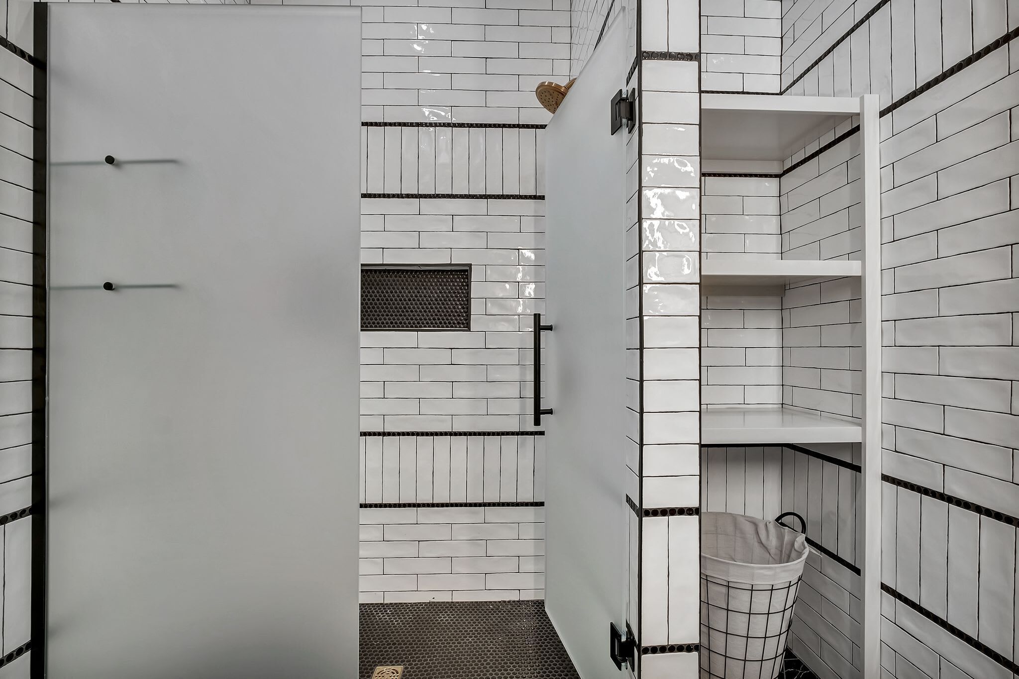Une salle de bain avec des murs carrelés de blanc, un espace douche et un panier à linge.