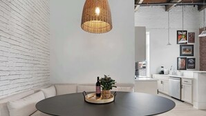 Una sala moderna con una mesa redonda, una lámpara colgante de mimbre, un sofá y una cocina al fondo.