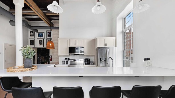 Una cocina moderna con gabinetes blancos, electrodomésticos de acero inoxidable y una isla grande con taburetes de bar.