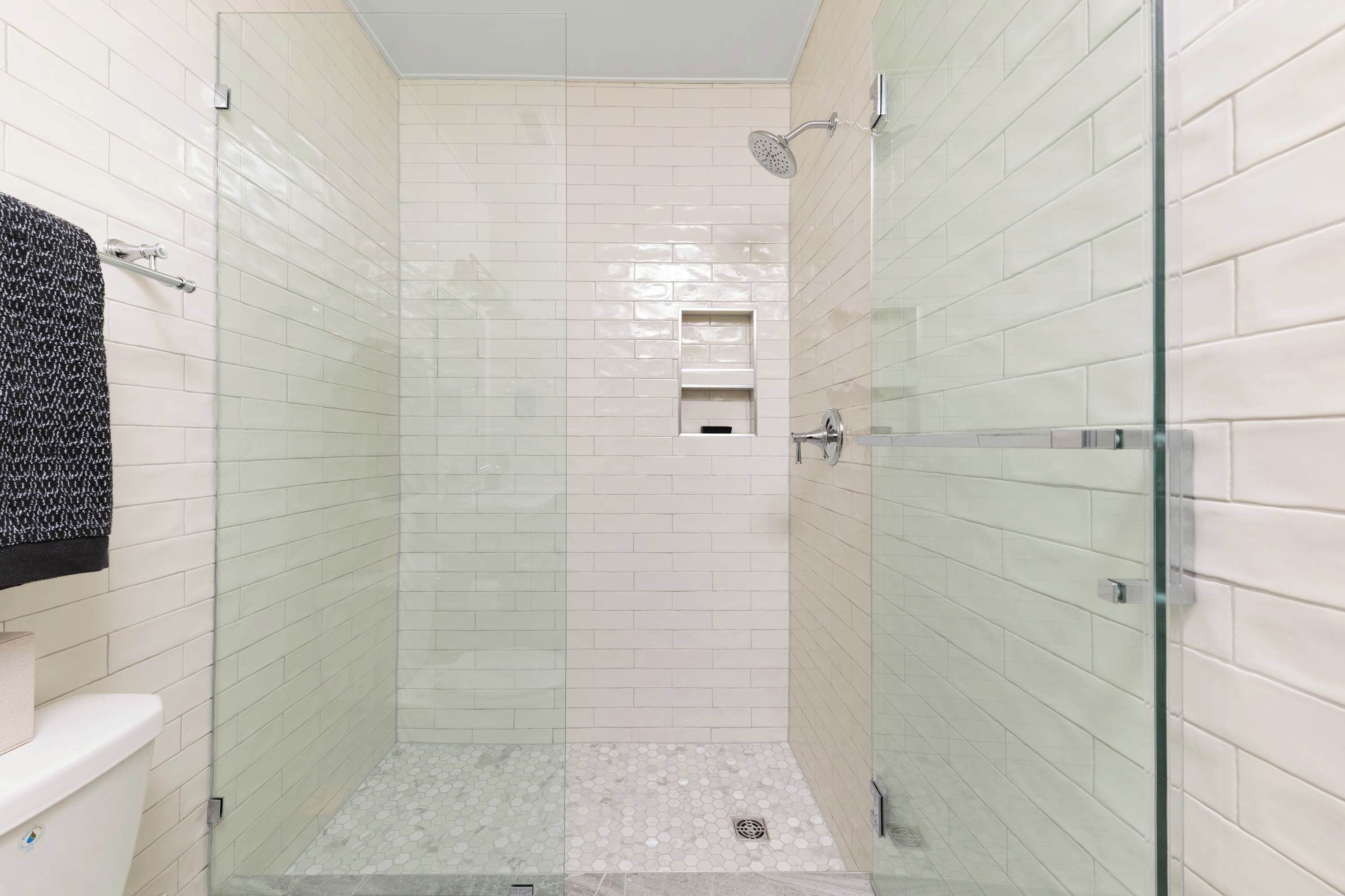 Un baño moderno con azulejos blancos tipo metro, un box de ducha de vidrio y un estante pequeño en la zona de la ducha.