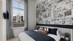 Un dormitorio moderno con una cama grande, un televisor montado en la pared y vista a la ciudad desde la ventana.