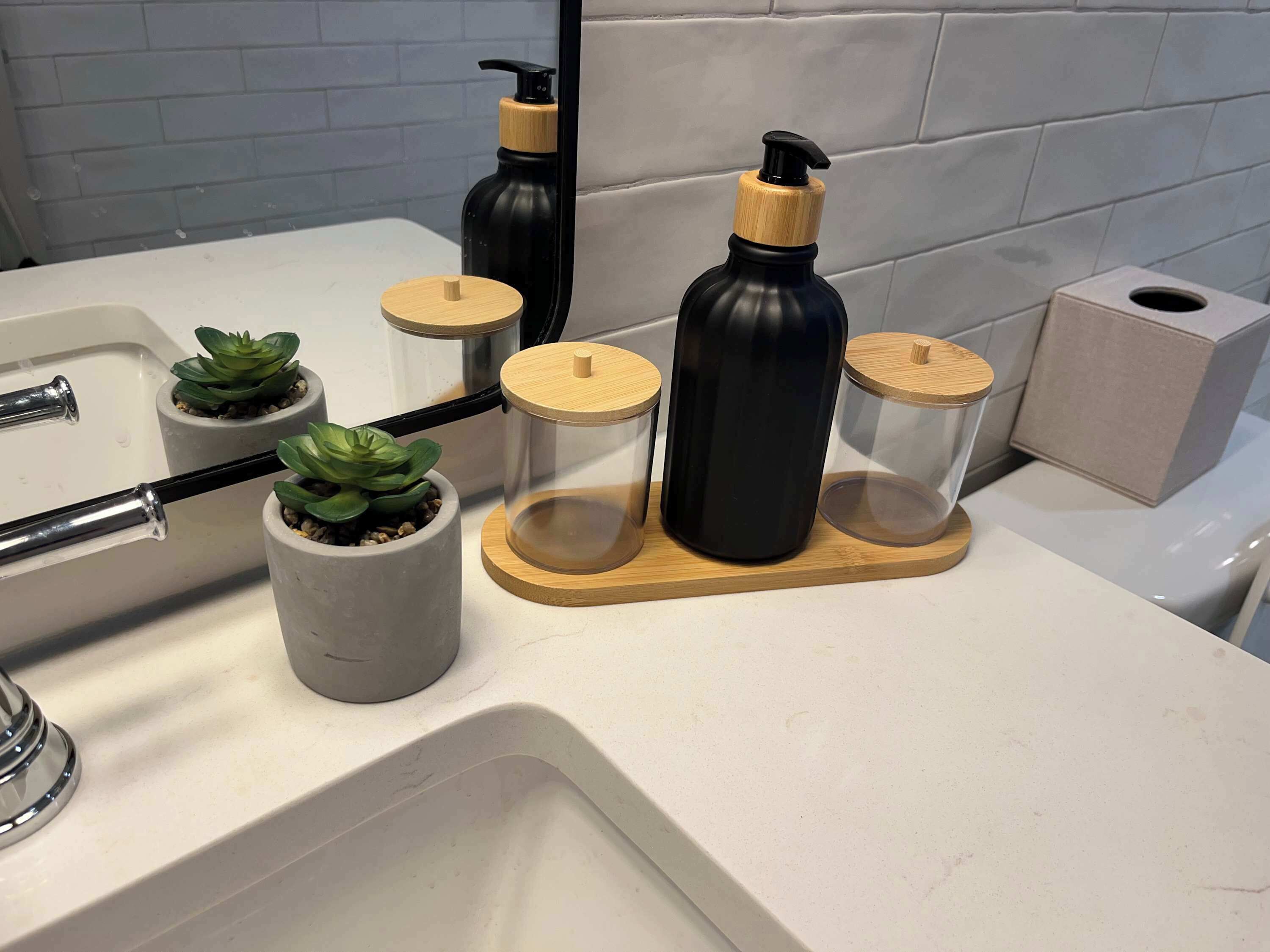 A bathroom with a white sink, two potted plants, and three black bottles with wooden lids on a wooden tray.