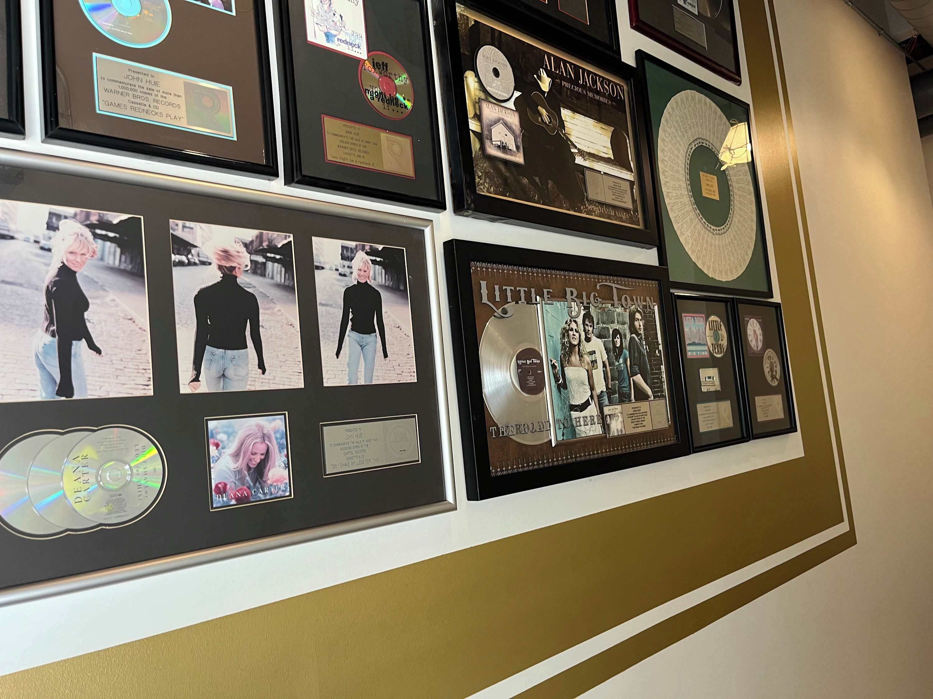 A wall displaying various framed items including CDs, photographs, and awards.