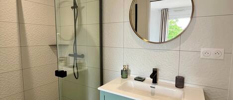A bathroom with a glass-enclosed shower, a white vanity with a round mirror, and a teal cabinet.