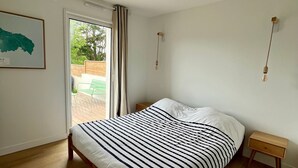 Un dormitorio con cama, mesita de noche de madera, luz de pared y ventana con cortinas.