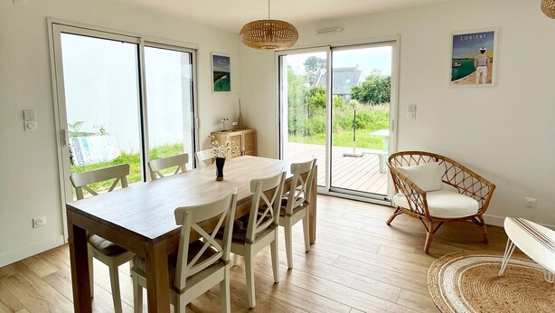 Un comedor con una mesa y sillas de madera, una silla de mimbre y vistas a un jardín a través de puertas de cristal.