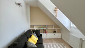 Una sala de estar moderna con un sofá negro, un tapete estampado y un estante blanco frente a un techo inclinado.