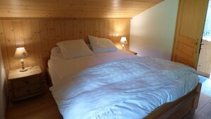 A bedroom with a wooden ceiling, a bed with white bedding, two bedside lamps, and a wooden wardrobe.