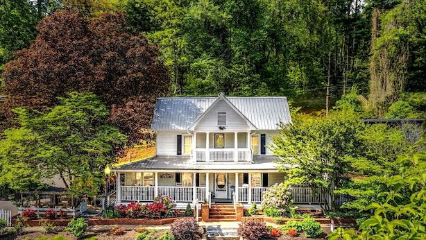 Ein zweistöckiges Haus mit einer Veranda, umgeben von einem Garten mit verschiedenen Pflanzen und Blumen.