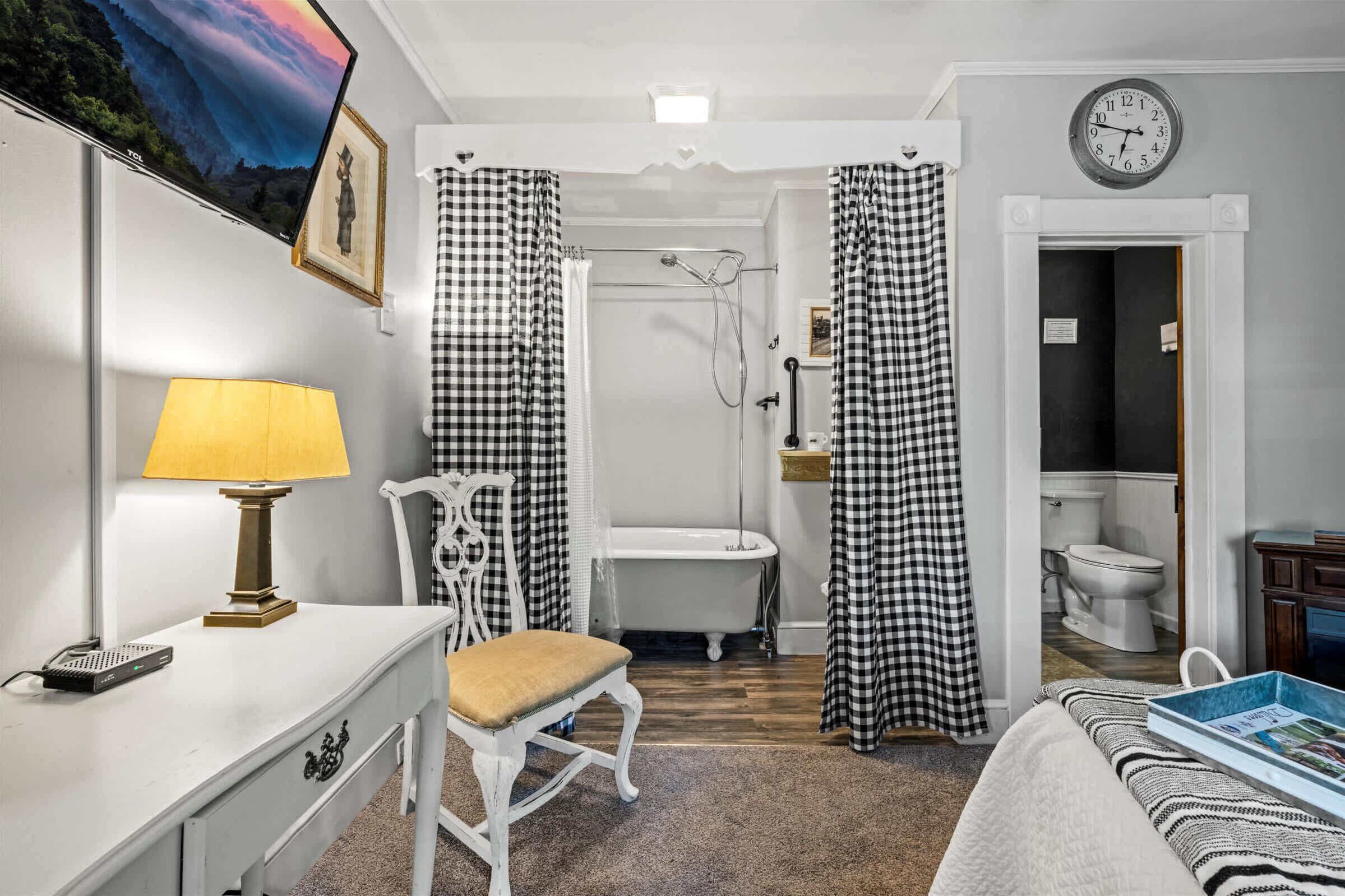 Een badkamer met een bad, toilet en douche. Op de muur hangt een klok en boven het bad is een televisie bevestigd.