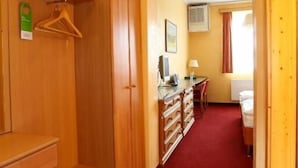 Habitación de hotel con armario de madera, escritorio con lámpara, cama y alfombra roja.