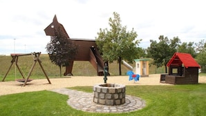 Un parque infantil con columpios, tobogán, una casita y una fogata.