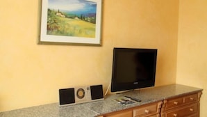 Una habitación con un cuadro de un paisaje enmarcado, un televisor de pantalla plana y un equipo de sonido sobre una encimera de granito.