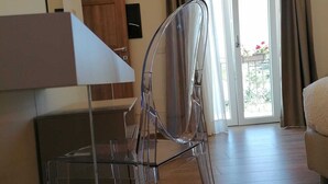 Una habitación con una silla de plástico transparente, piso de madera, una mesa blanca y un gran ventanal corredizo que da al exterior.