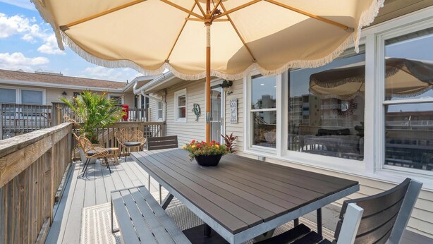 A wooden deck with a table and chairs, a large umbrella, and a potted plant. - Cozy Oceanblock Condo - Steps To The Beach (Ocean City)