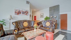 A modern living room with a leather sofa set, a coffee table, and a red ottoman. There is a painting on the wall and a plant in the corner. - Collection O near Terminal Pulo Gebang formerly Sentra Timur - Tower Sapphire (Jakarta)