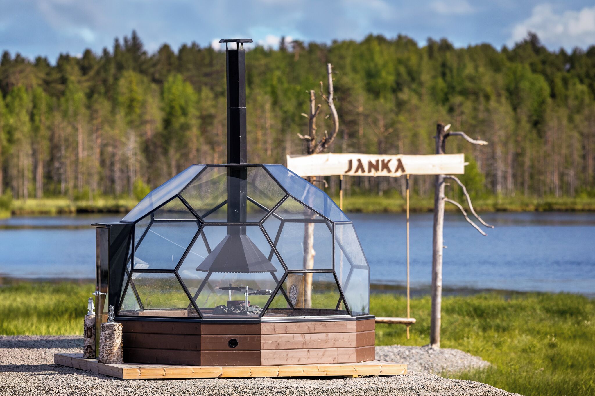 Une structure en forme de dôme géodésique, dotée d’une cheminée, est installée sur une surface de gravier. On peut voir, en arrière-plan, une enseigne sur laquelle est écrit le mot « JANKA ».