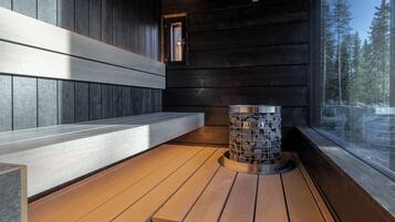 Houten blokhut interieur met een bank, een stenen pilaar en een raam met uitzicht op een bos.