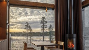 A modern interior with a large window, a fireplace, and a dining area. - Jänkä Resort (Äkäslompolo)