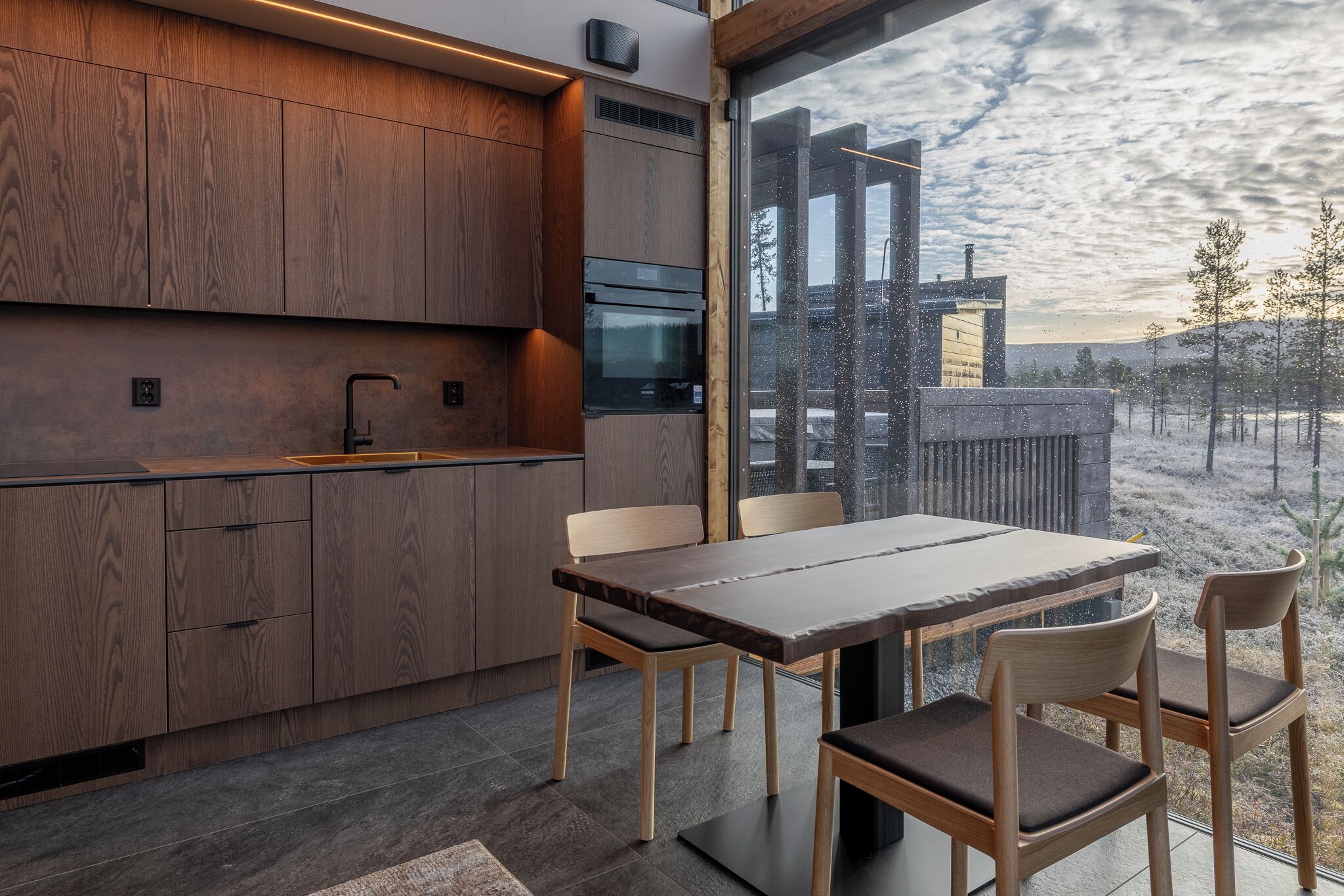 Una cocina moderna con armarios de madera y un ventanal con vistas a un paisaje nevado.