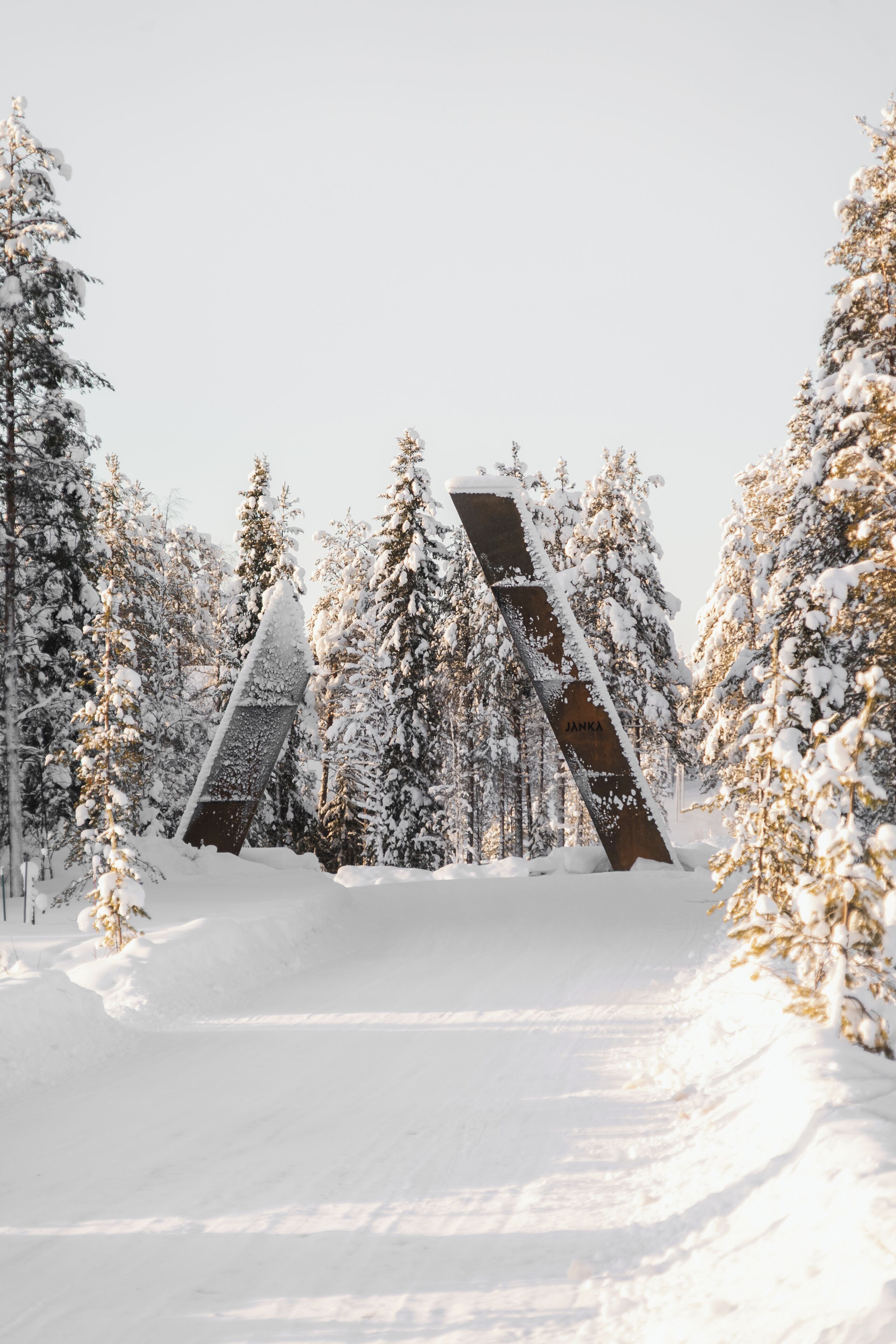 En snötäckt stig leder fram till en byggnad där inskriptionen ”JANKA” syns, och allt detta omgivs av en skog med snötyngda träd.