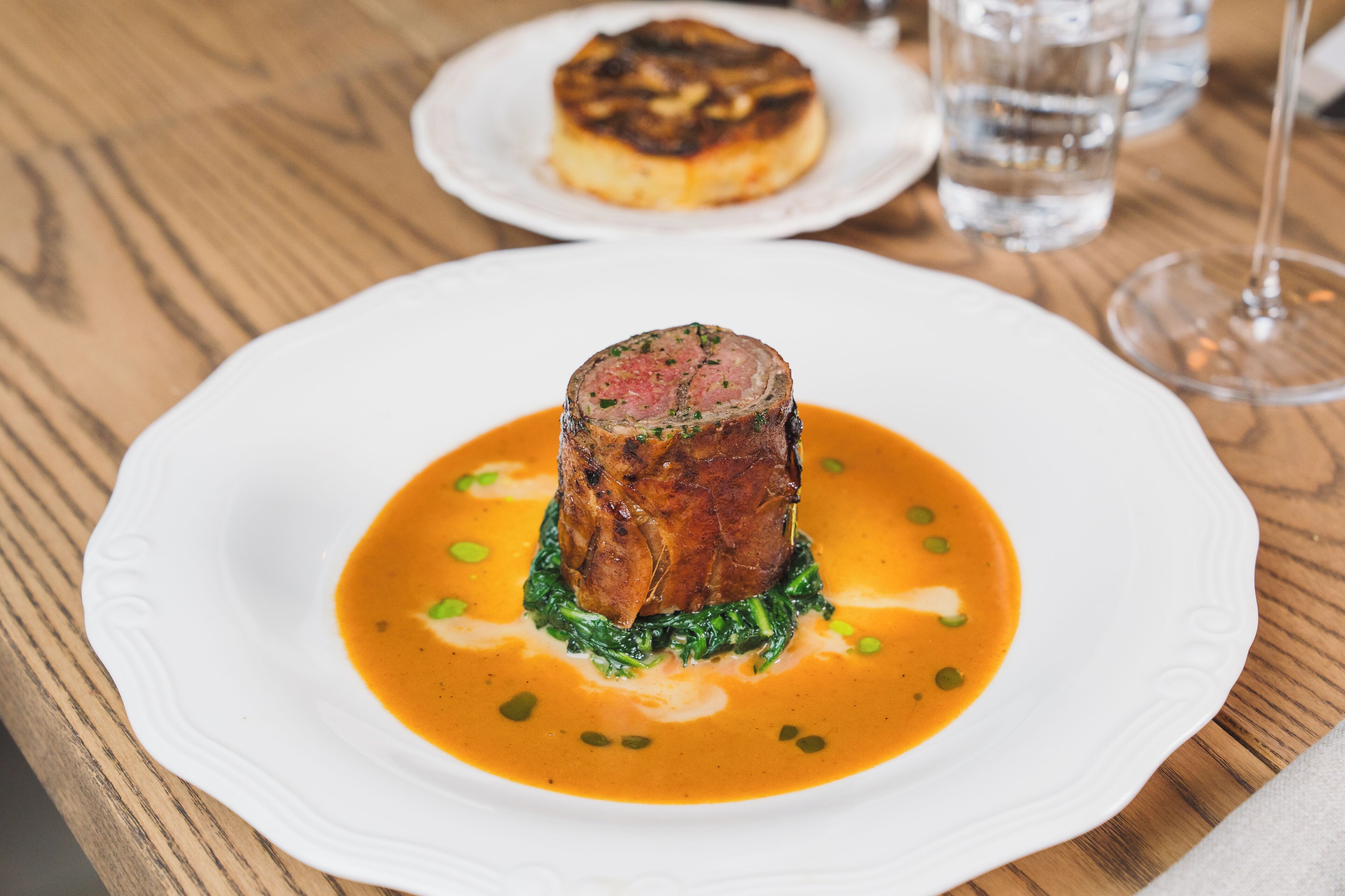 A plate with a meat dish and sauce, a glass of water, and a wine glass on a wooden table.