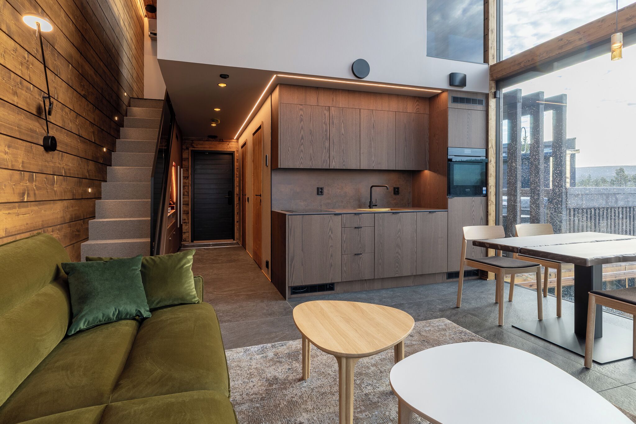 A modern kitchen with wooden cabinets, a dining area with a table and chairs, and a green sofa with cushions.