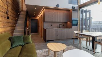 A modern kitchen with wooden cabinets, a dining area with a table and chairs, and a green sofa with cushions.