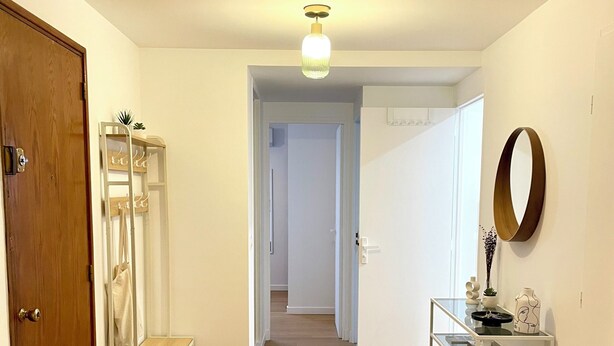 Un pasillo con una puerta de madera, un estante blanco con adornos y un espejo en la pared.