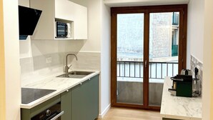 Una cocina moderna con horno empotrado, microondas y fregadero. Hay una puerta corrediza de vidrio que da a un balcón con vistas a la ciudad.