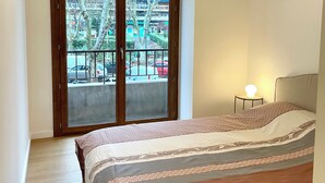 Un dormitorio con cama, mesita de noche, lámpara y vista a un edificio a través de una puerta de cristal.
