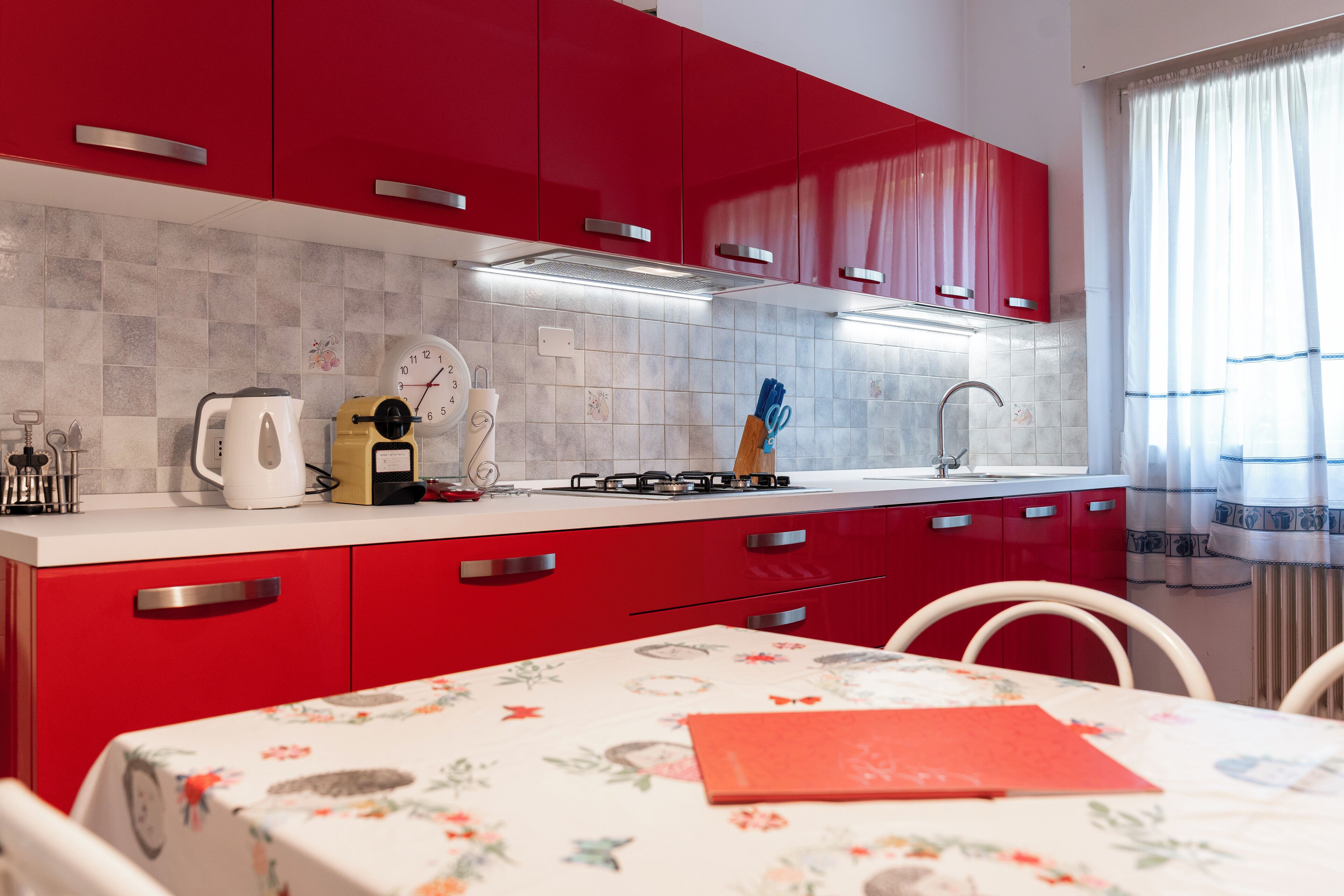 A modern kitchen with red cabinets, a white countertop, and a clock.