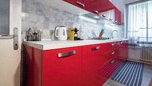 A modern kitchen with red cabinets, a white countertop, and a tiled backsplash. - Ca' Orso Marino (Venice)