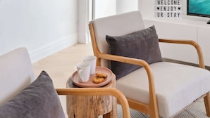 Un rincón acogedor con una silla de madera, una pequeña mesa redonda con una bandeja que sostiene una taza y galletas, y un letrero en la pared que dice 'WELCOME ENJOY UR STAY'.