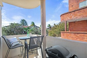 A balcony with outdoor seating, a grill, and a view of a brick building and trees. - Cosy Curlewis - Walk to beach - New Listing (Bondi Beach)